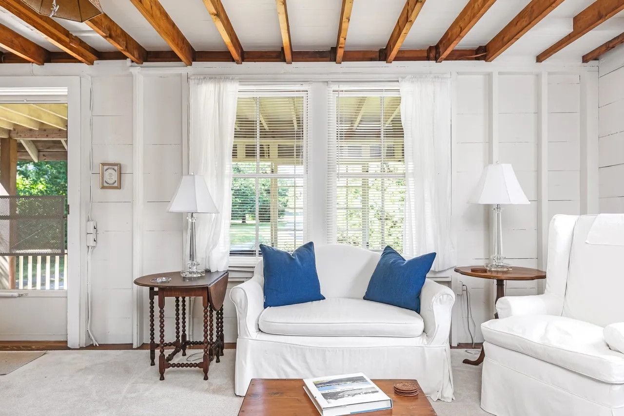 Interior of a cozy sitting room in the $12.2m Watch Hill mansion, featuring rustic exposed beamed ceilings and abundant natural light from period windows.