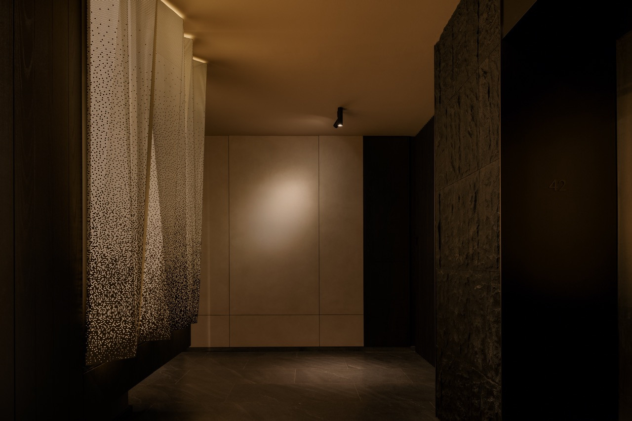 View from the lift lobby entrance showing the custom perforated metal light installation with concealed dimmable LED lighting