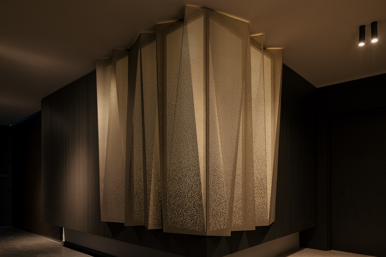 The origami-like light installation in brushed Chardonnay gold is composed of folded perforated metal sheets with a dissolving gradient pattern