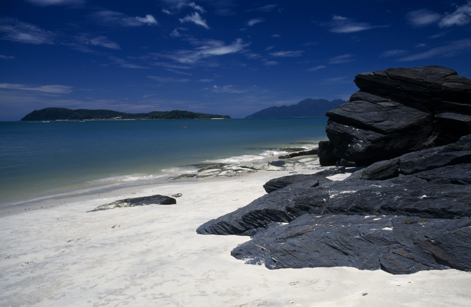 Malaysia, Kedah, Langkawi, Pantai Tengah beach looking towards Pulau Rebak Besar island with rocks in the foreground.(Photo by: Eye Ubiquitous/Universal Images Group via Getty Images)