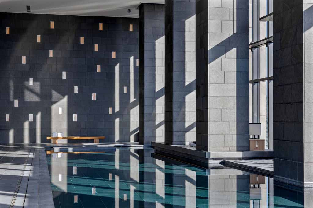 In daylight, the water surface reflects shifting skies and subtle architectural lines, reinforcing the pool’s meditative calm