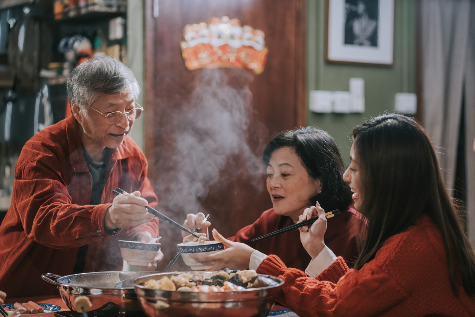 Senior man passing food to daughter in law during Chinese New Year family reunion dinner hong kong multi generation family having family reunion dinner at home (ภาพ: Edwin Tan / Getty Images)