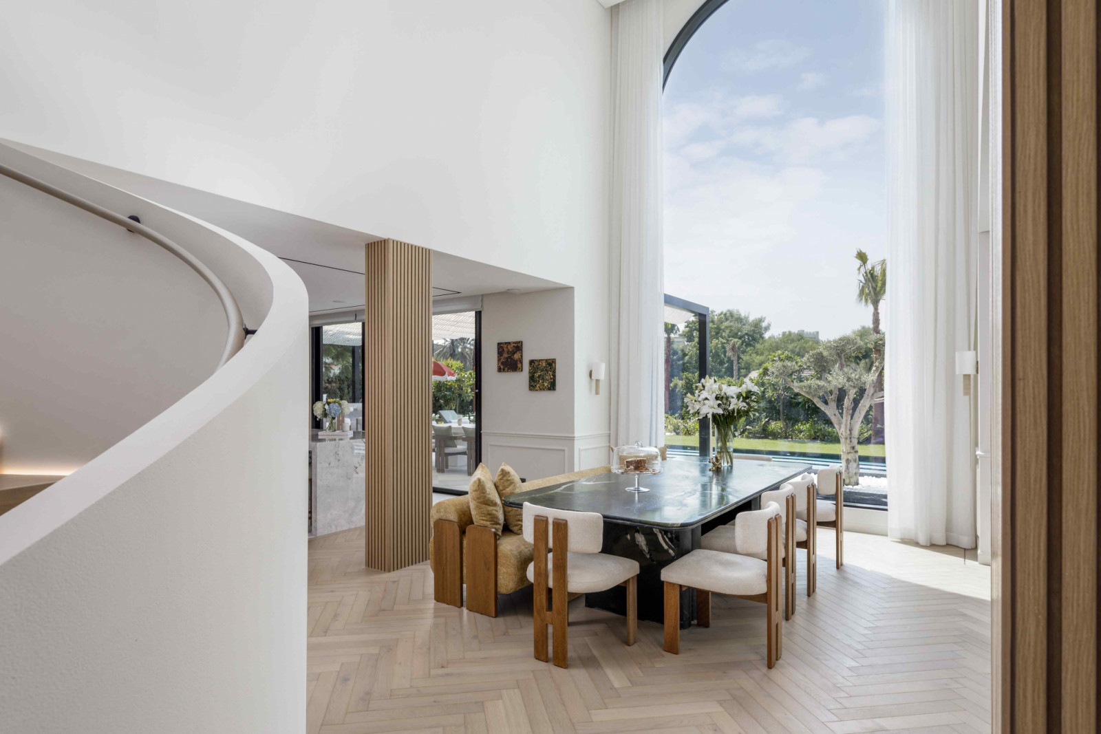 The dining area beneath a soaring floor-to-ceiling glass façade overlooking the pool and garden