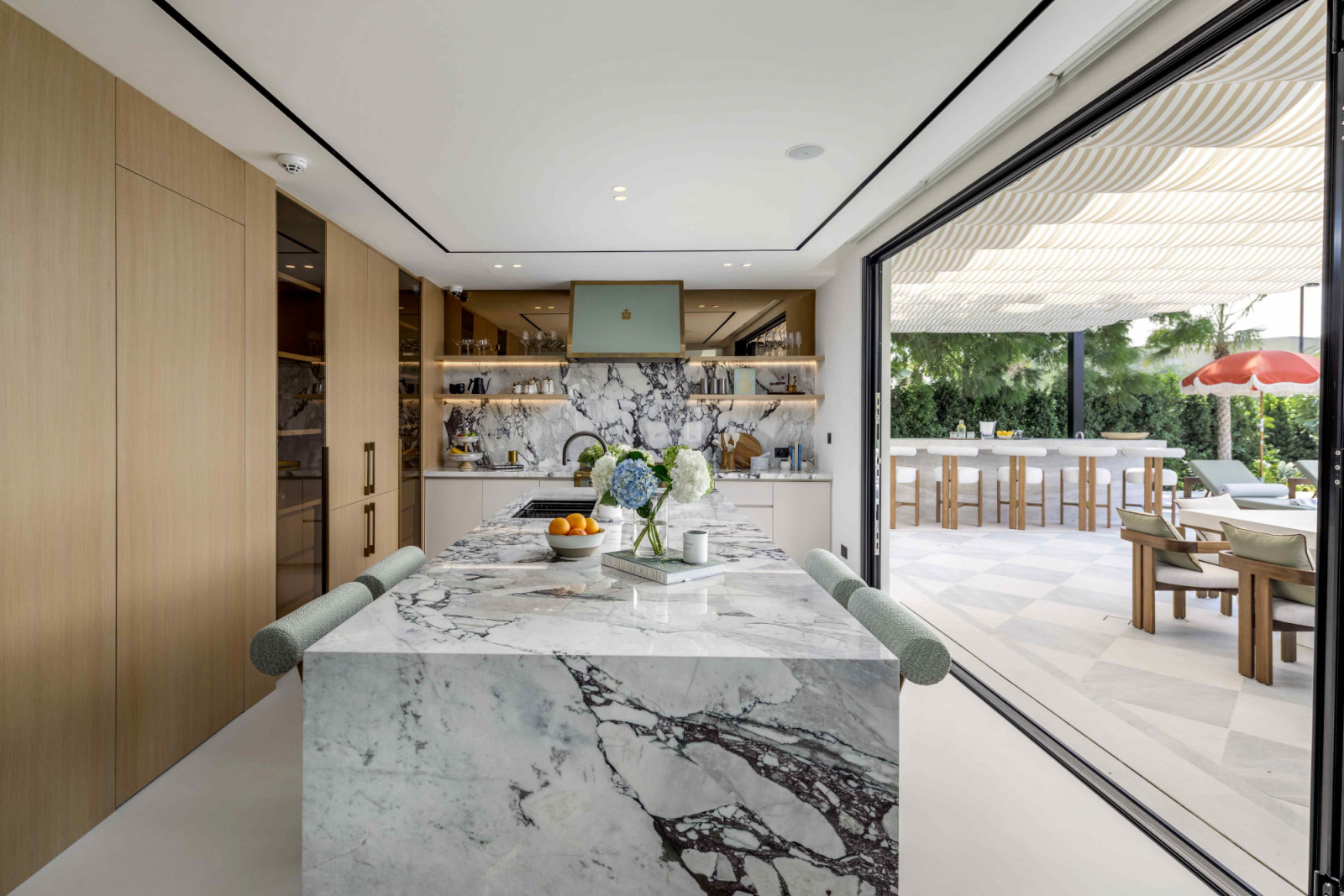 The kitchen opens onto a tropical-inspired outdoor terrace through large bi-folding doors