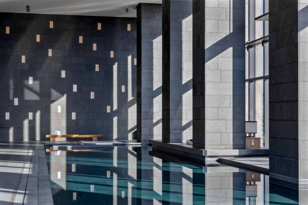In daylight, Aman Tokyo spa pool’s water surface reflects shifting skies and subtle architectural lines, reinforcing the pool’s meditative calm