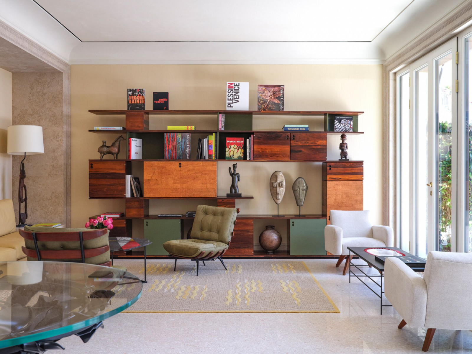 Mid-century modern shelving systems display contemporary art books and African sculptures, referencing the Dolce Vita era when this film hotel became synonymous with Venice Film Festival glamour