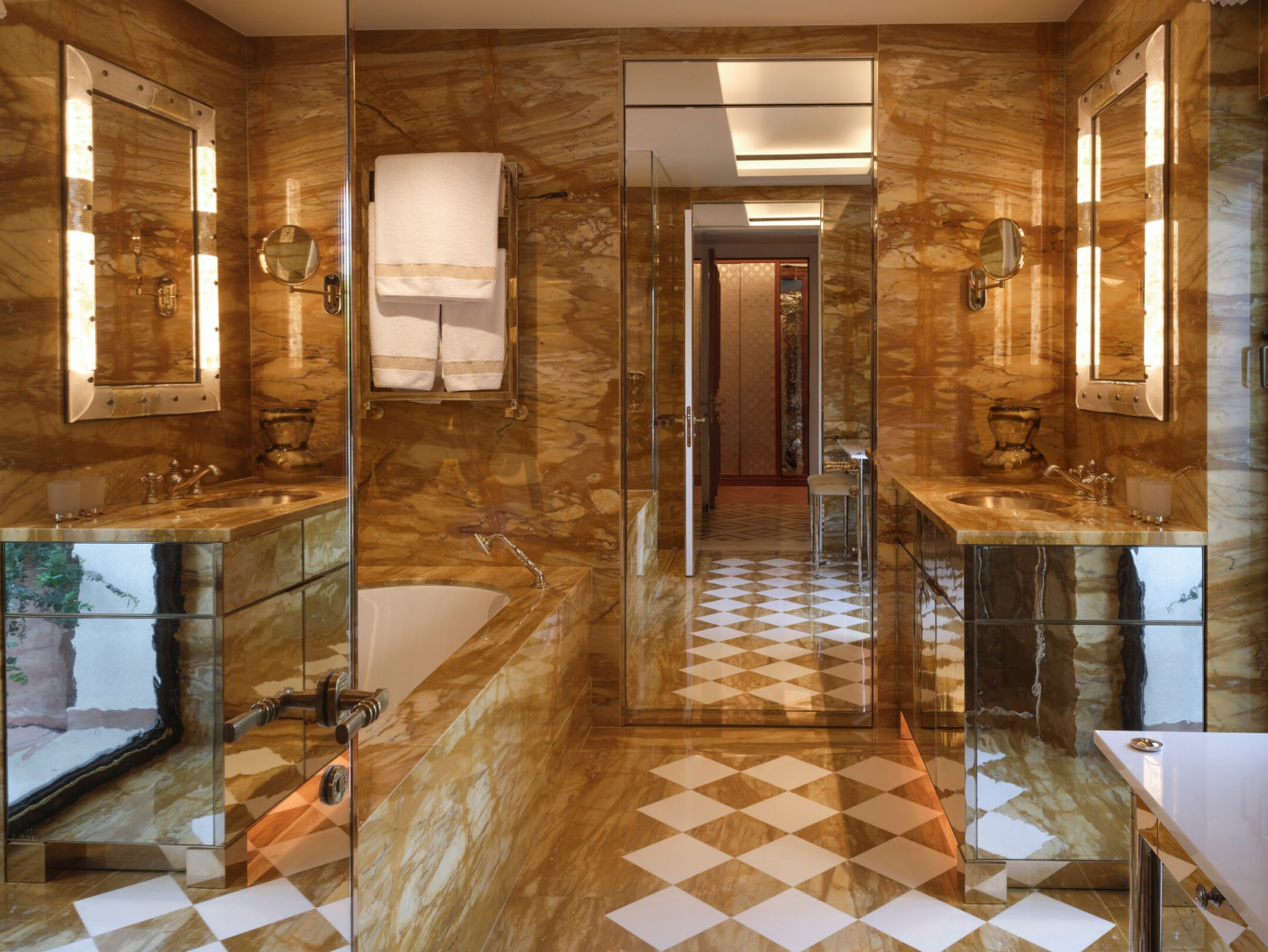 Book-matched honey onyx marble wraps the master bathroom, featuring dual vanities and custom lighting, in one of the film hotel’s reimagined suites