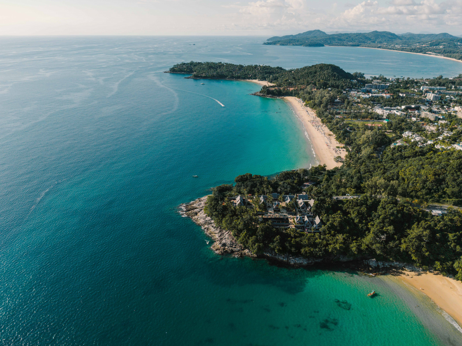 An aerial view of Phuket’s west coast, where forested headlands and pale sandy beaches meet the open expanse of the Andaman Sea