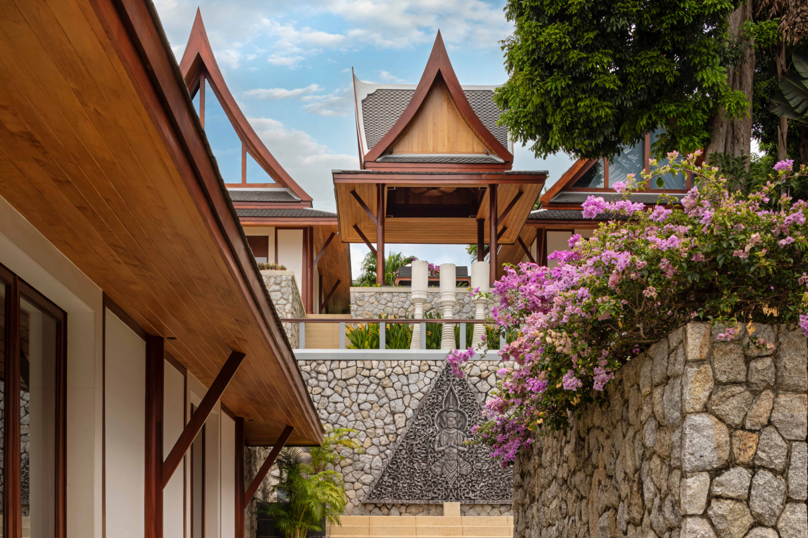 An alleyway between buildings evokes a quiet, village-like atmosphere, finished in natural stone and softened by lush bougainvillea spilling between levels