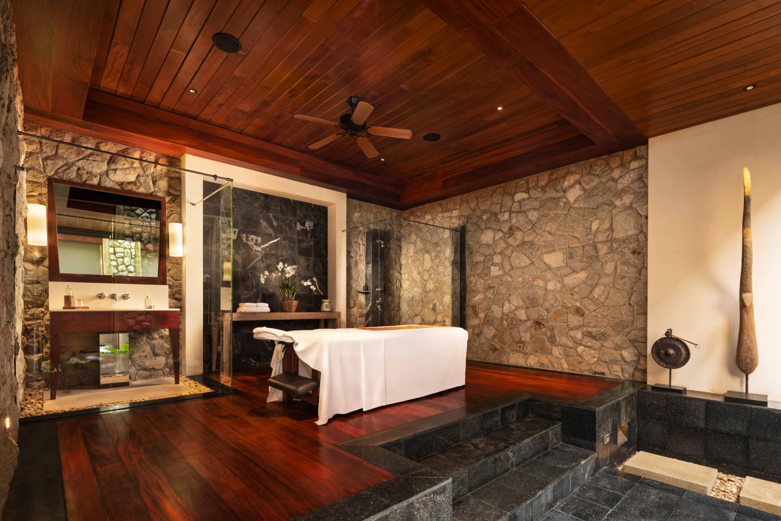 Outdoor massage area featuring a dark-toned material palette of timber, stone and black stone riles, creating a cocooning atmosphere