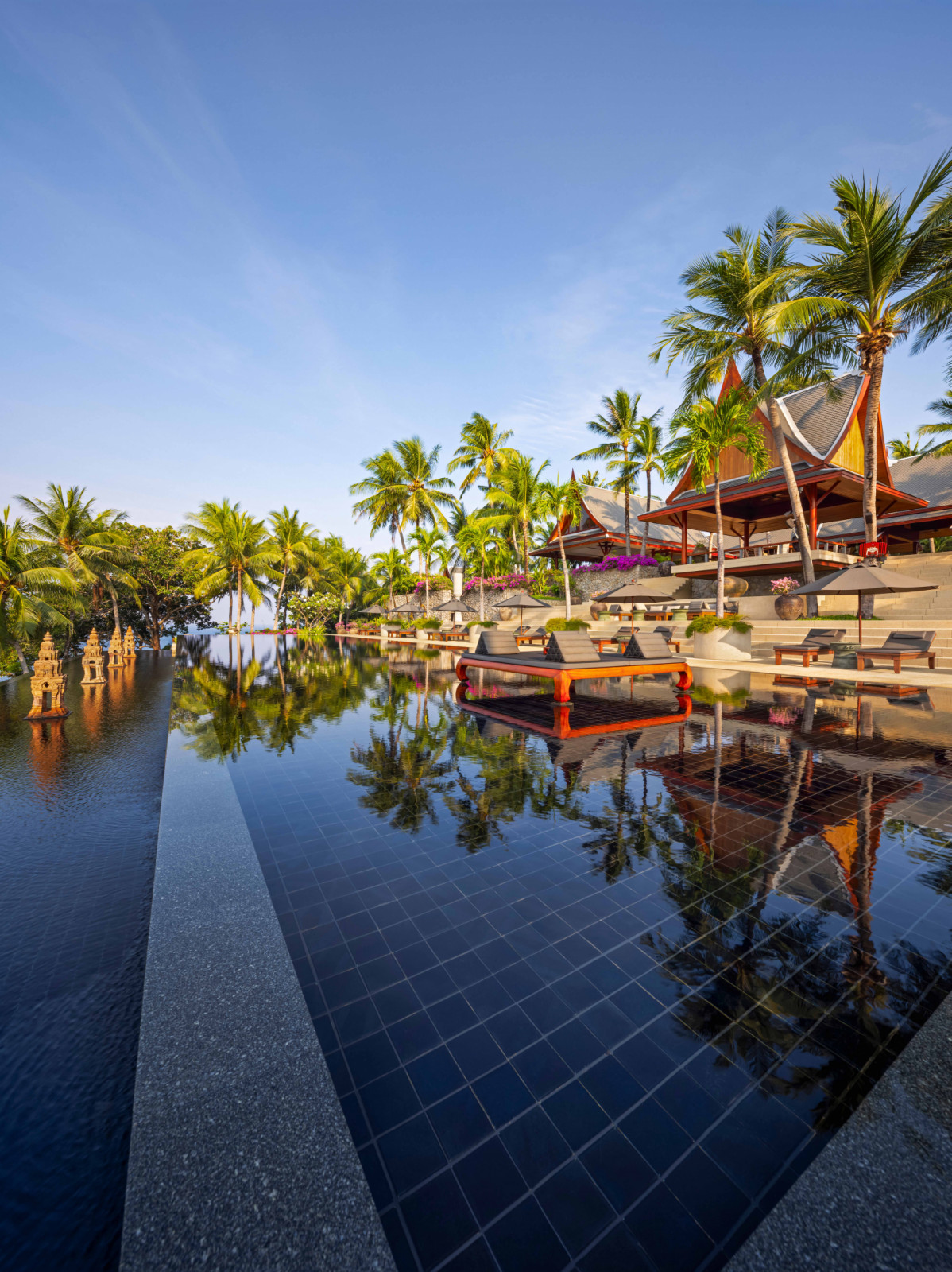 A black-tiled pool installed with an ornate daybed captures the full resort spirit of the estate, where water, palms and architecture come together in a single, expansive setting