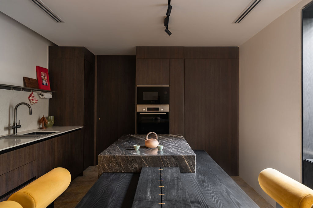 The kitchen's black quartzite island extends to meet a black-stained dining table, forming the centre of the social core