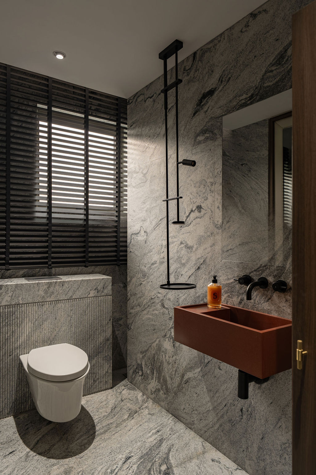 Black horizontal louvres filter light into the ground-floor bathroom, where Viscount White granite walls meet a custom terracotta vanity