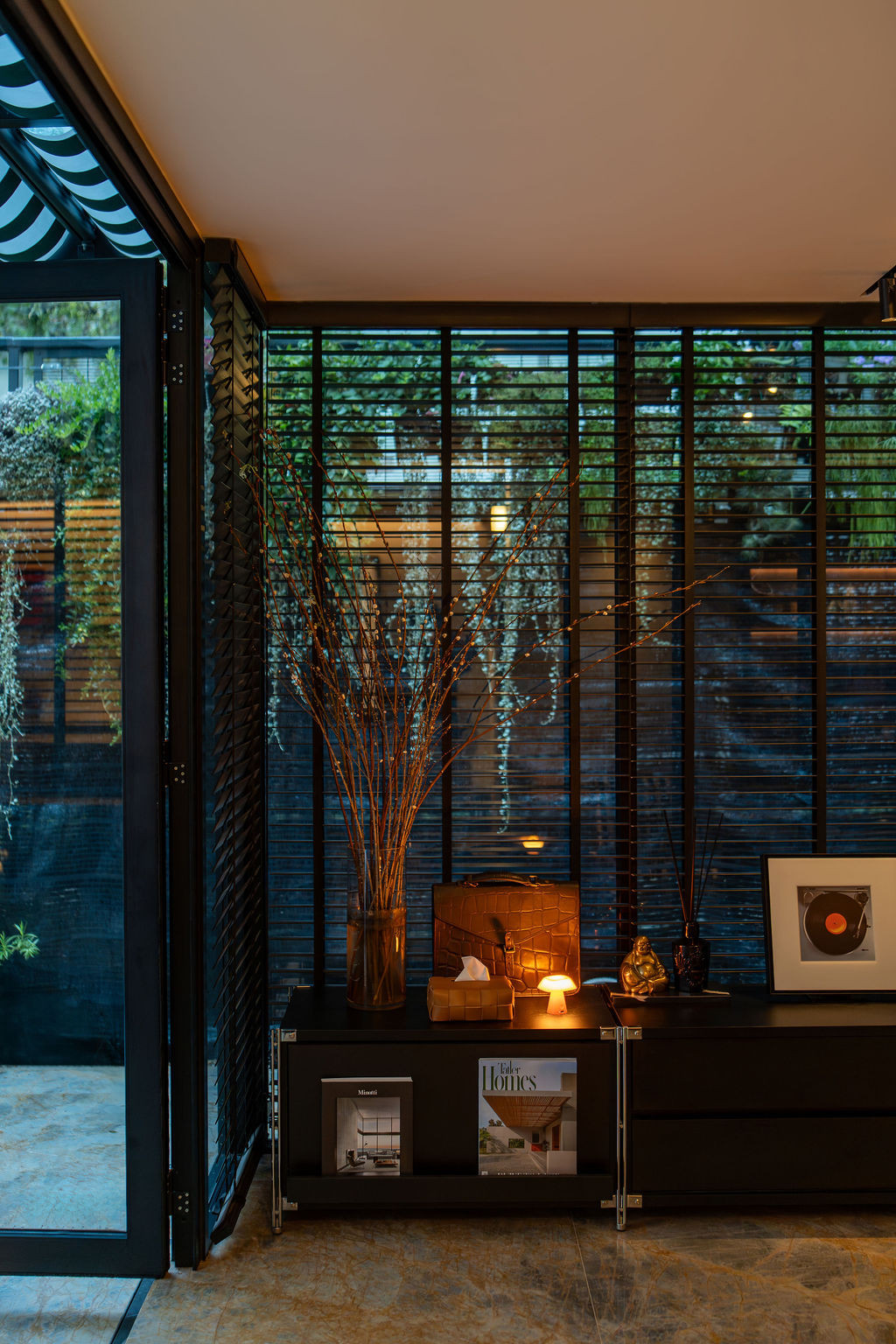 Controlled lighting transforms the atmosphere at night, with black-framed doors opening to the garden beyond