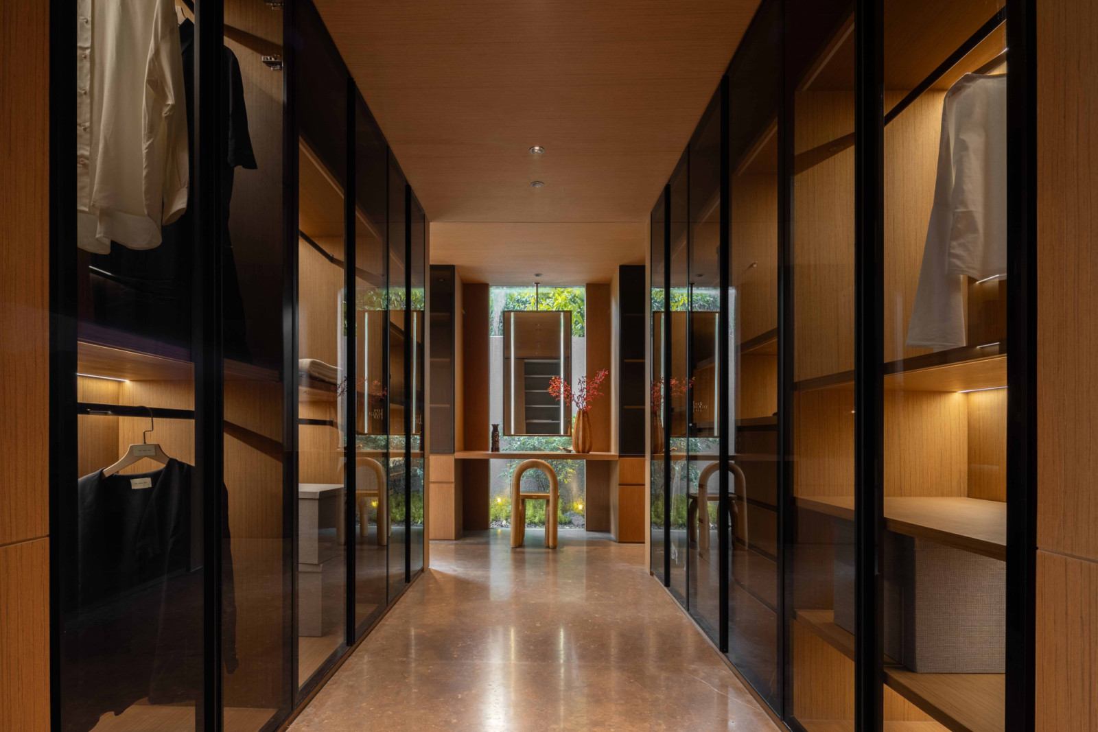 A double-bay walk-in wardrobe on the ground floor is conceived as a linear passage, framed by glass-fronted cabinetry and a warm timber lining