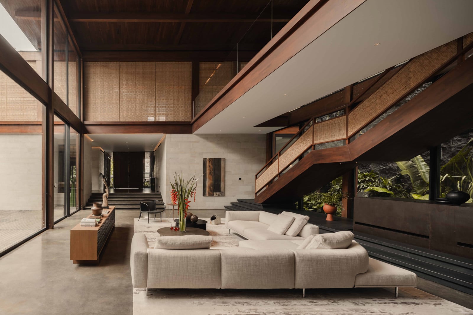The Interwined Residence’s double-height living room in daylight reveals layered circulation, with the staircase and upper bridge overlooking the shared space