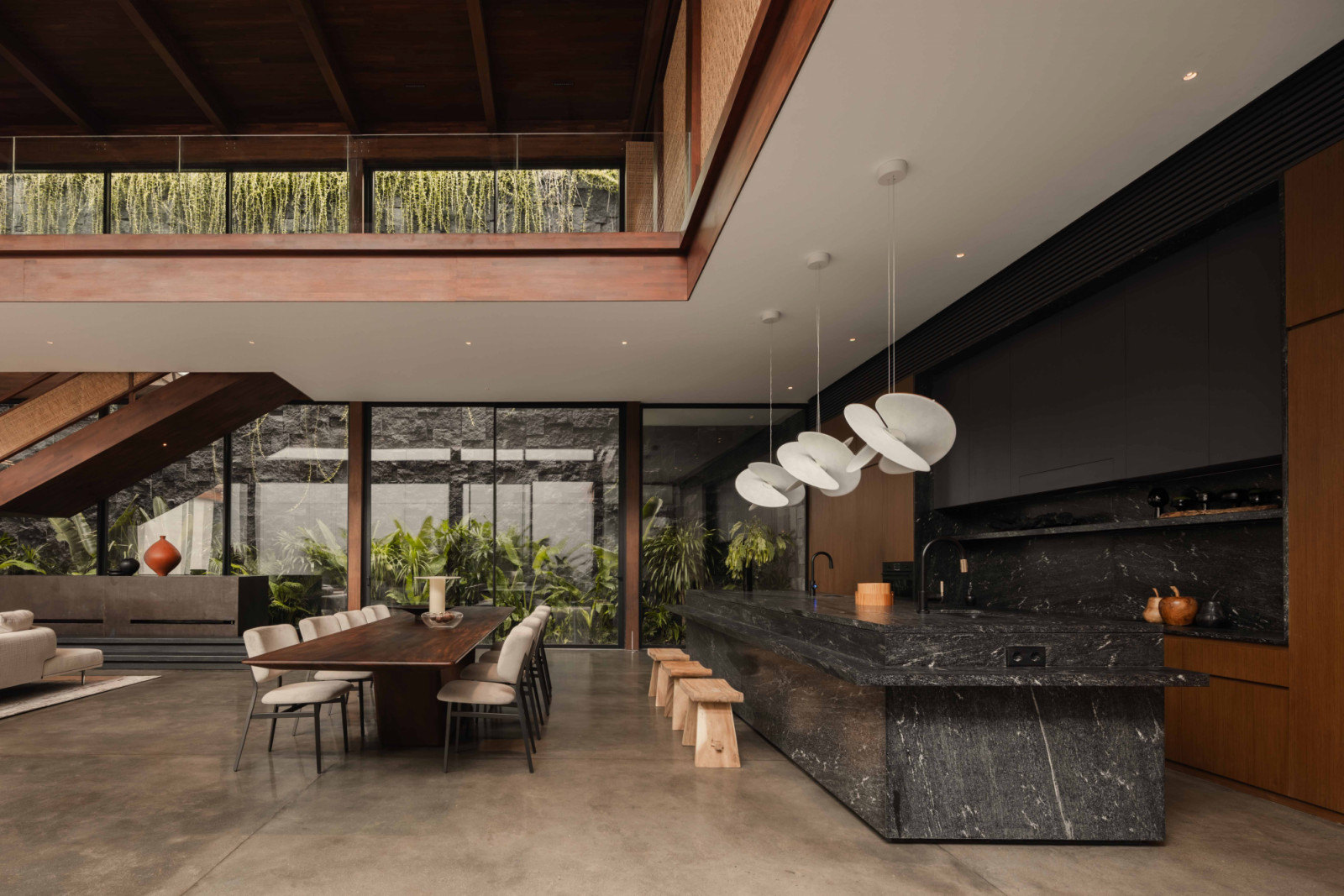 A dark-toned kitchen overlooks the double-volume living space, where timber and white-painted surfaces create contrast