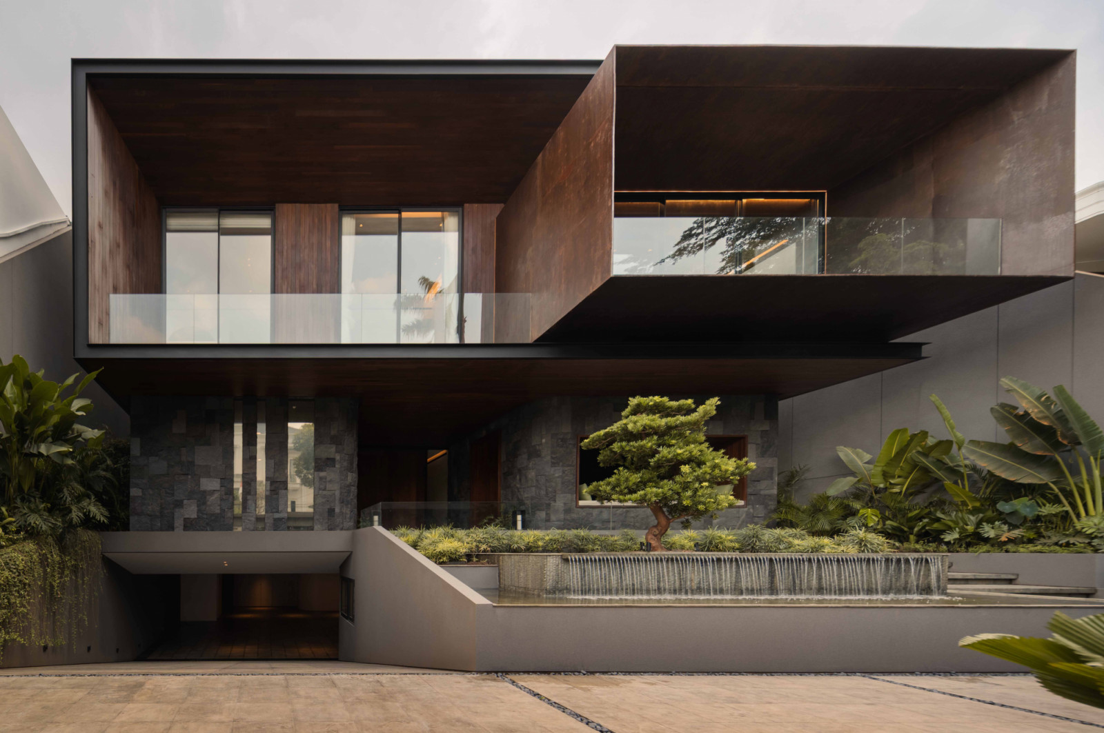 The front landscape of the Intertwined Residence is tiered with reflecting pools and a bonsai focal point, creating a spa-like arrival sequence that eases the transition from work to home