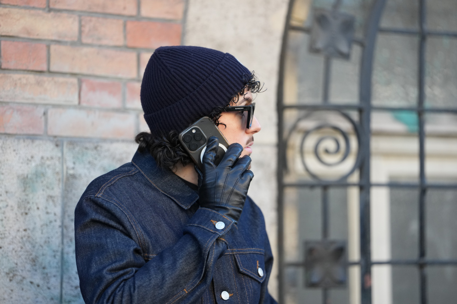 PARIS, FRANCE - JANUARY 24: A guest wears short black curly hair under a black knit beanie, black rectangular sunglasses, a dark blue indigo denim jacket with a pointed collar, black shiny leather gloves, outside Magliano, during Paris Fashion Week - Menswear Fall/Winter 2026-2027, on January 24, 2026 in Paris, France (Photo by Edward Berthelot/Getty Images)