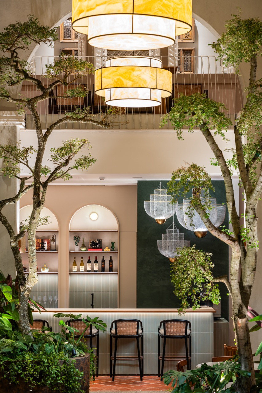The bar opens to the courtyard, where bonsais function as living sculptures and arches frame views across multiple levels of the interior spaces