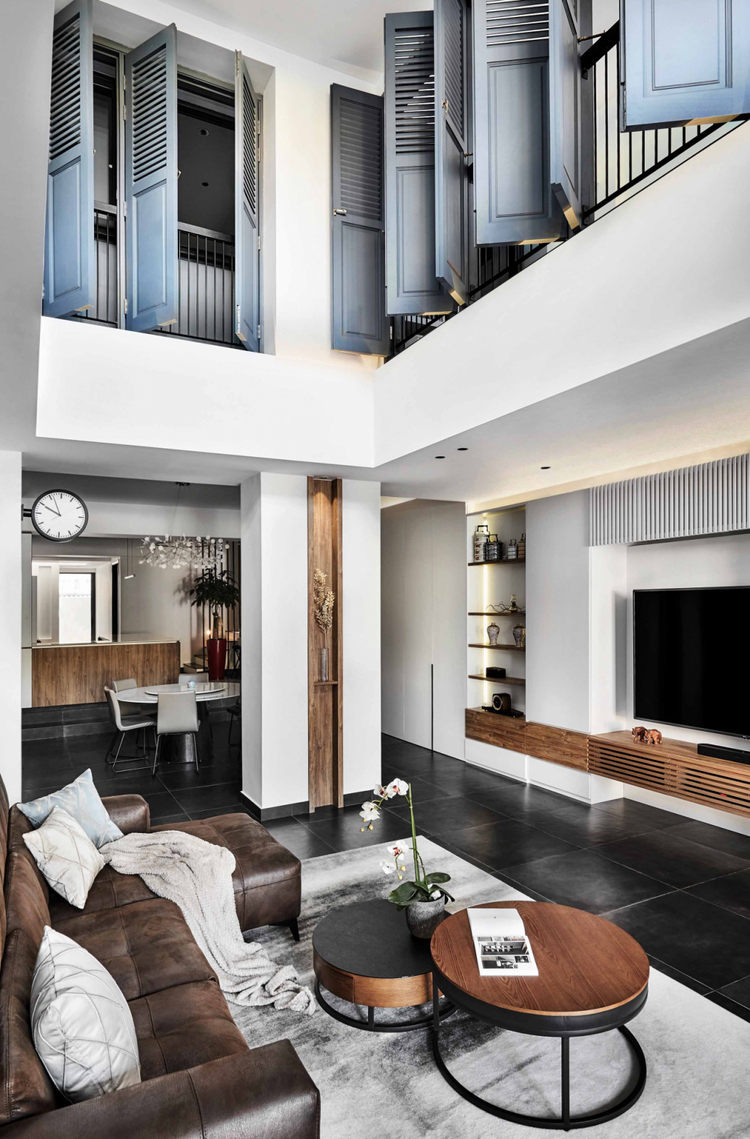 The living room of this Siglap terrace house by AMP Design Co features a double-volume ceiling lined with grey, louvered Peranakan-style casement windows