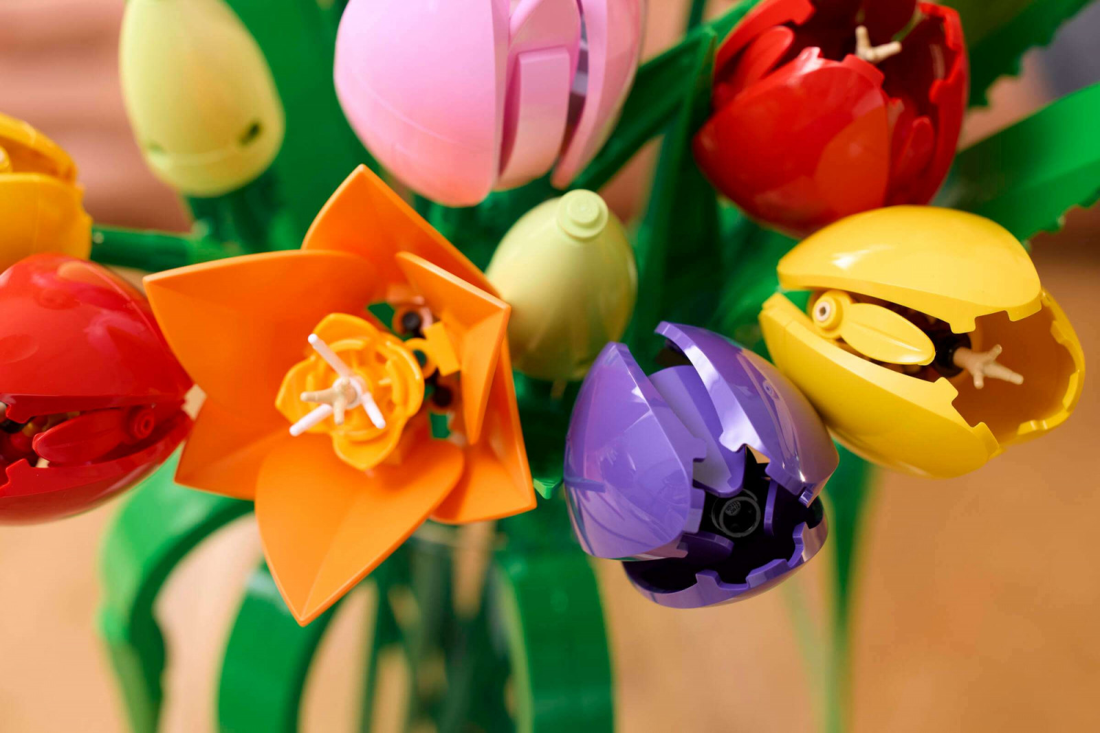 The open lily-flowering tulip variety in orange, alongside closed buds in purple and yellow. The open flowers use a different construction technique, with flat petal pieces clipped outward from a central stamen built from existing Lego elements