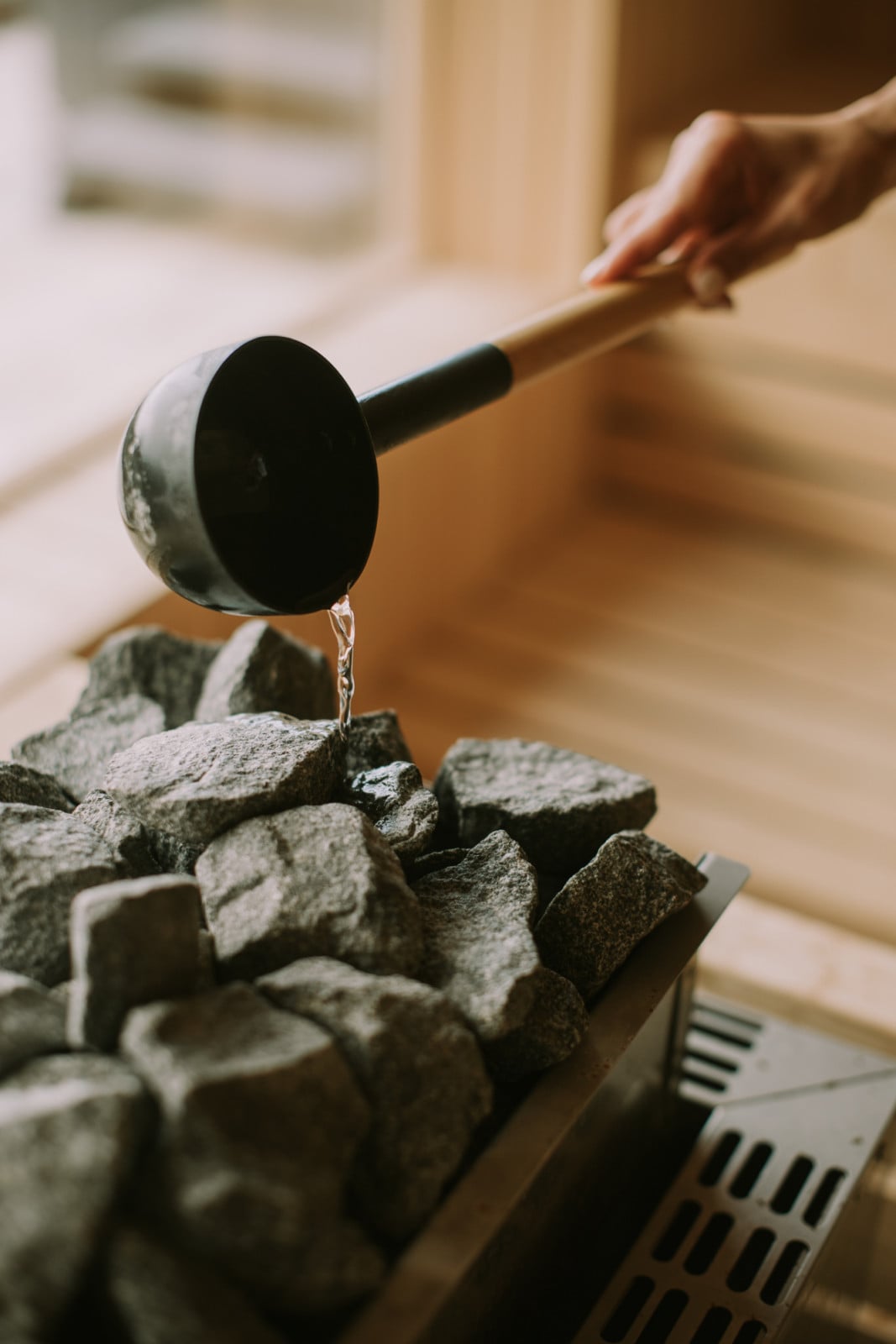 Young woman hand pouring water on hot rocks in the sauna