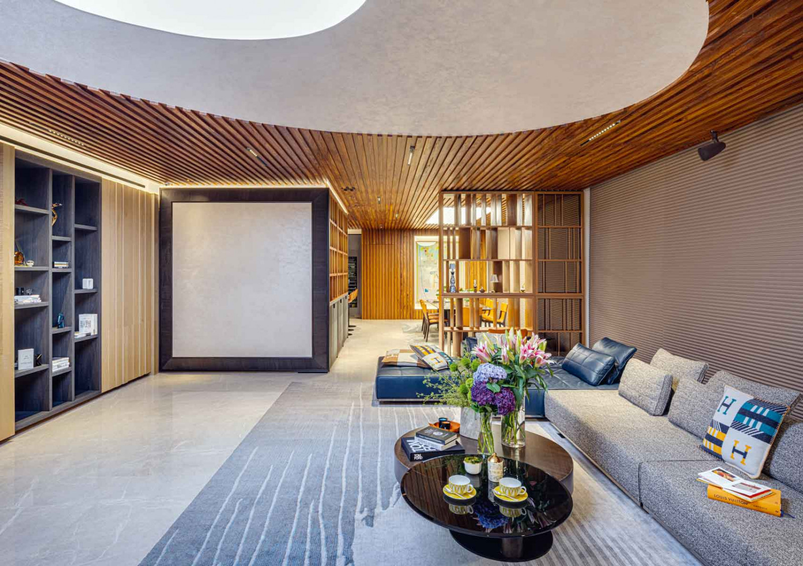 The dramatic yet inviting living space flows seamlessly into the dining area, separated by a sculptural copper screen that also doubles as a display case