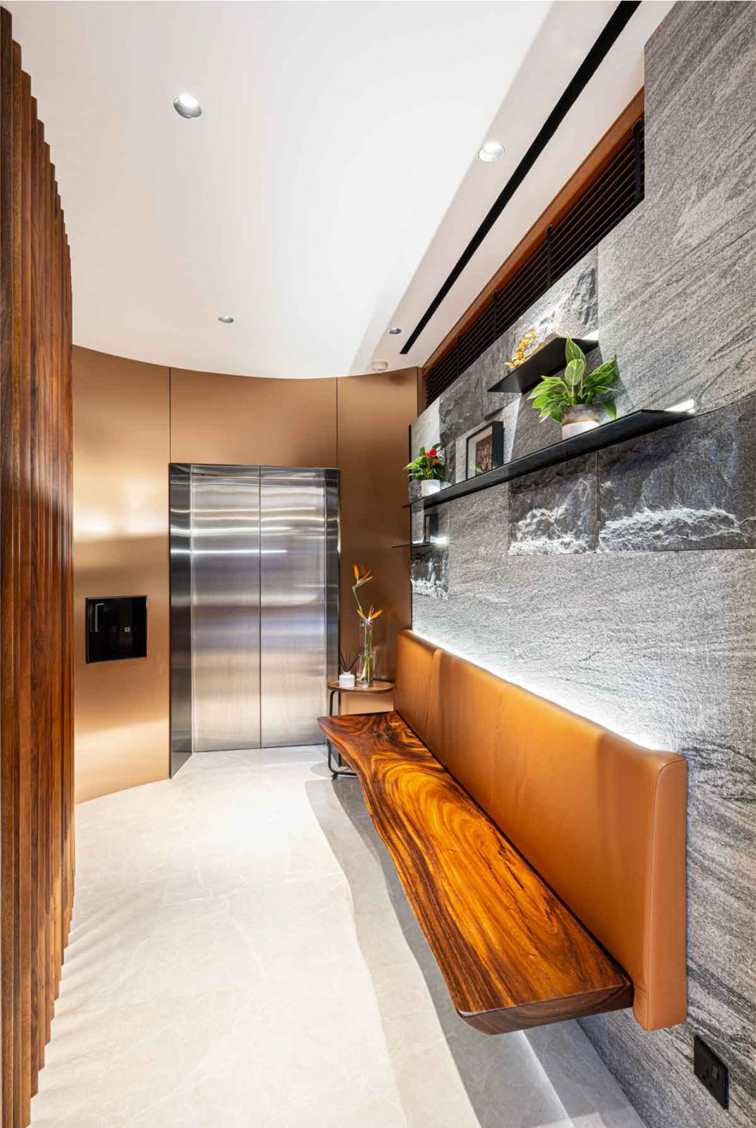 The curved bronze screen and stone surfaces in the lift lobby create a sense of arrival
