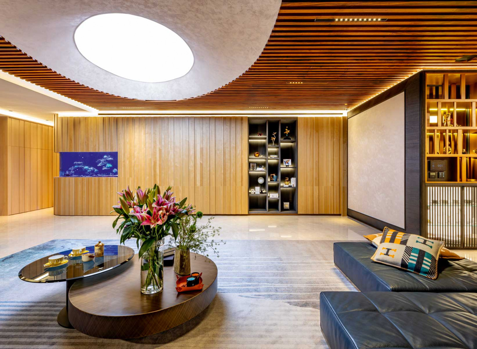 The circular ceiling feature in the living room acts almost like a skylight, drawing the gaze upwards while the rounded aquarium introduces movement and life at eye level