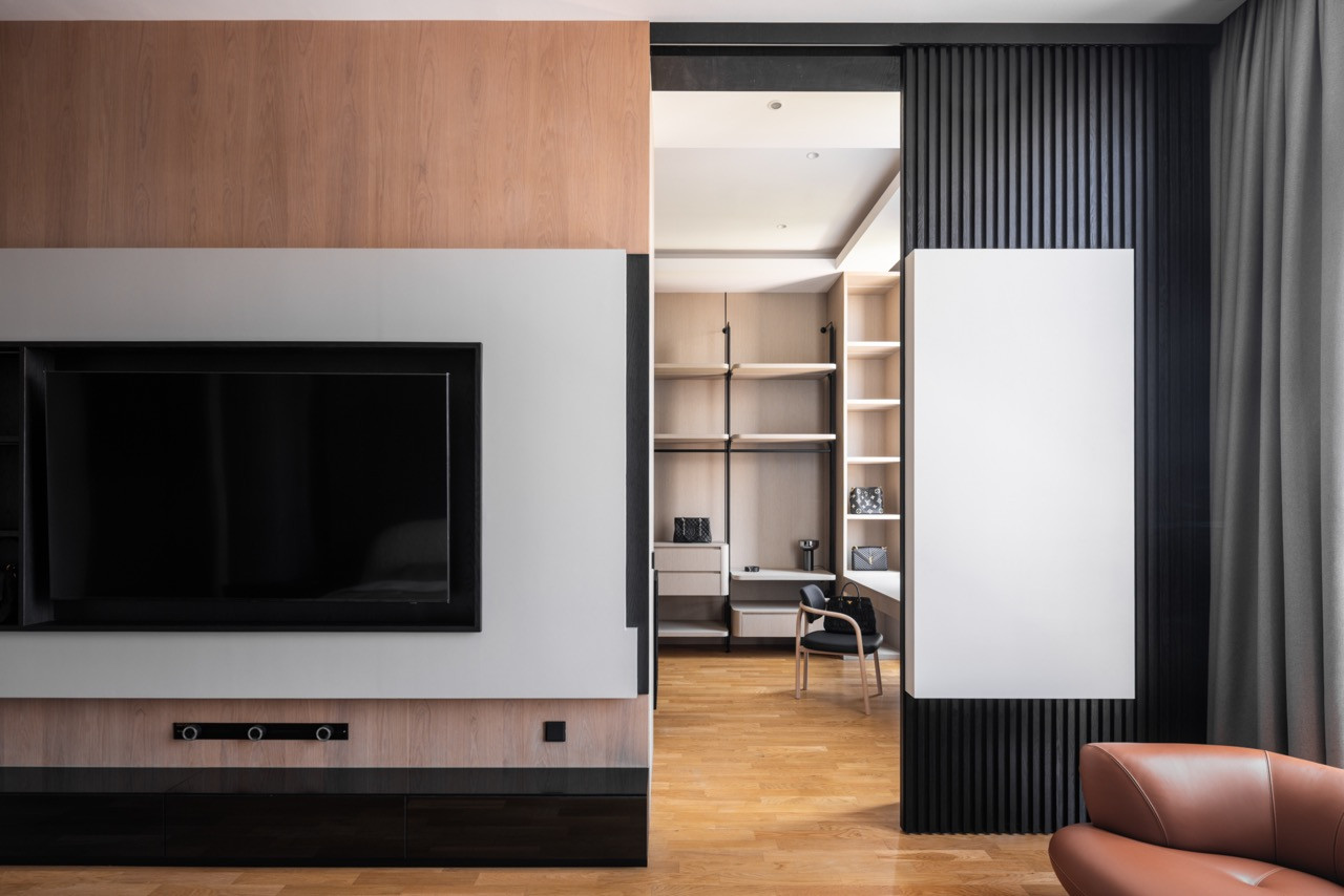 The master bedroom television wall in light oak and white lacquer, with the walk-in wardrobe visible through the open sliding door to the right, framed by dark fluted timber cladding