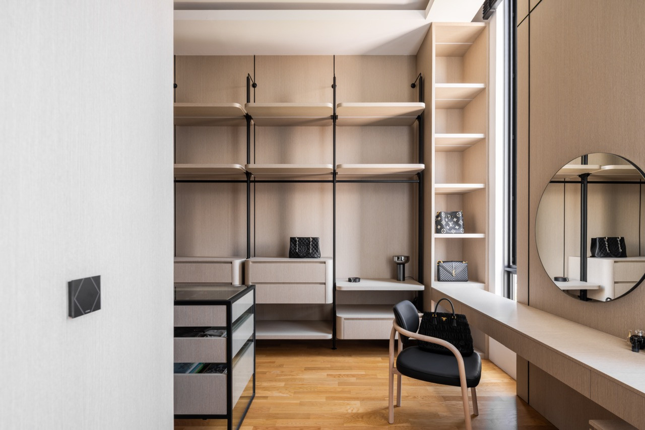 The master walk-in wardrobe from the entrance, with a full-width open shelving system in light timber and black steel, a built-in vanity desk, and a circular mirror to the right