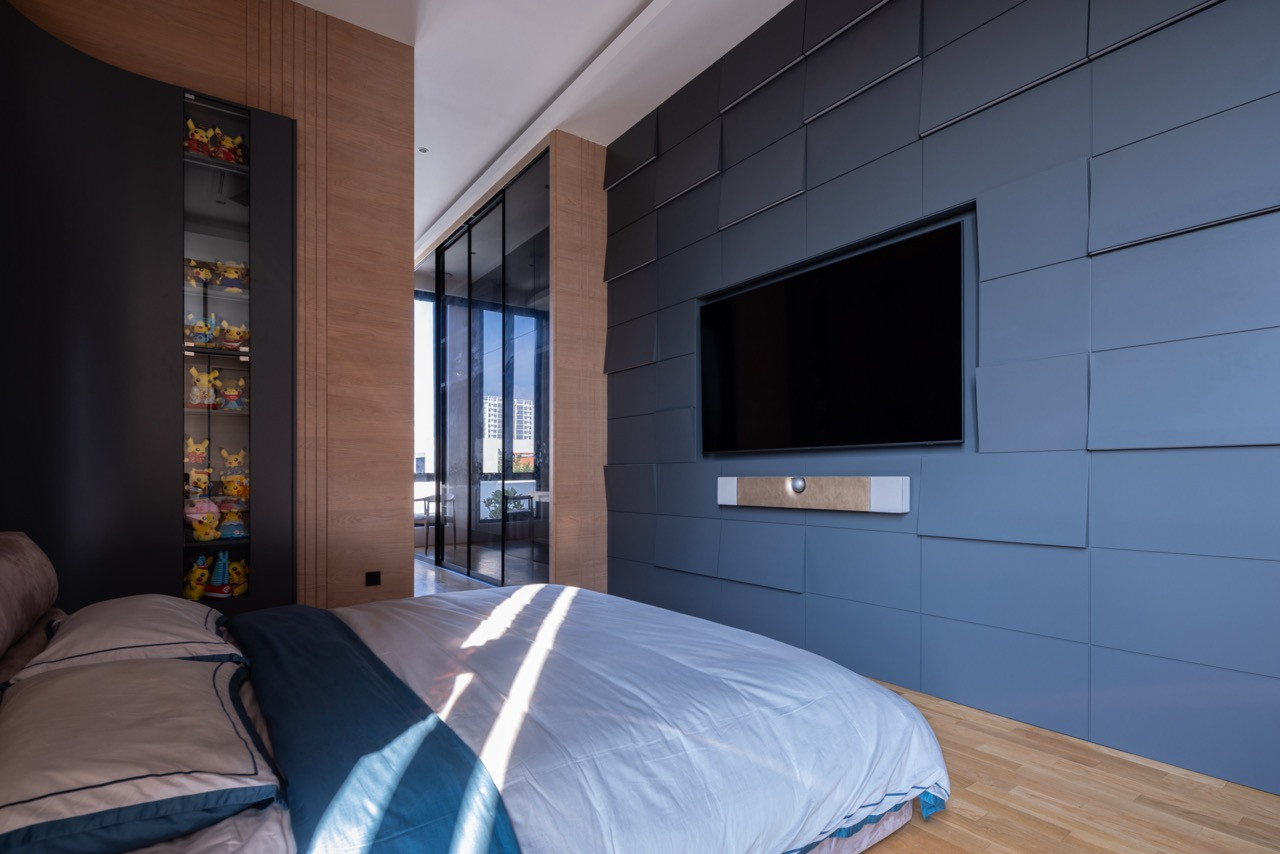 One of the bedroom suites, with a wall of matte slate-blue padded panels housing the television