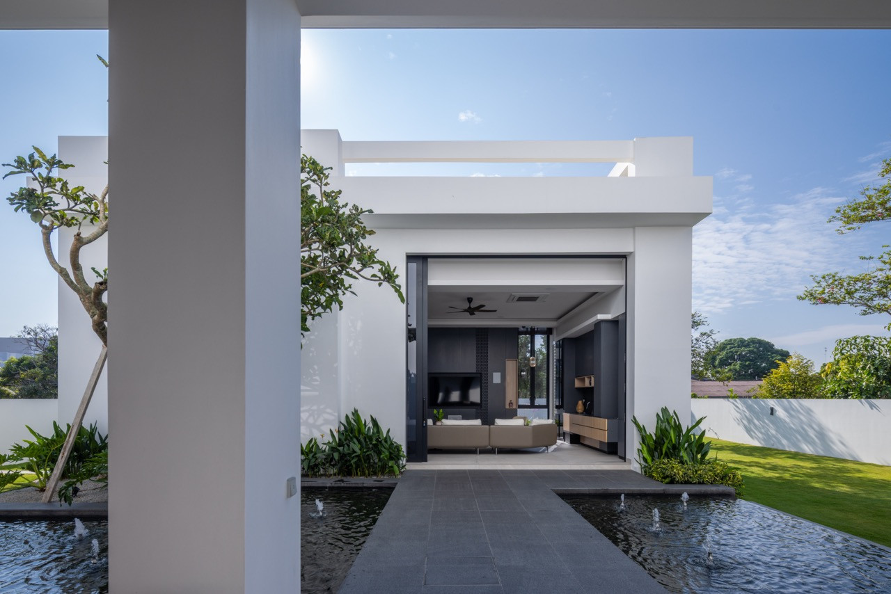 The rear villa is seen from across the second water pond, with a stone-paved path running between the pond's fountain jets toward the open bifold entrance