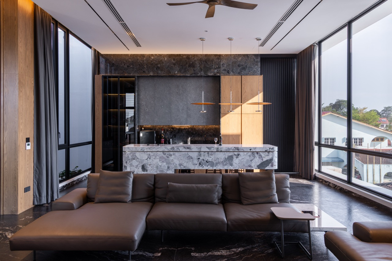 The family room on the upper floor, open to the Muar skyline through full-height glazing on three sides, with the Ori Grey and Argos Black kitchen island at rear