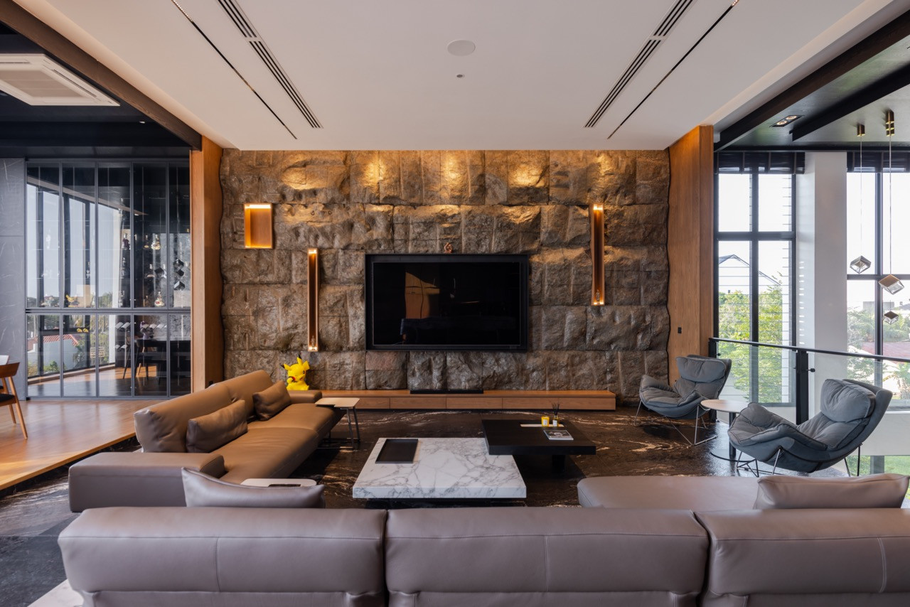 The living room, viewed from the dining wing, shows the granite television wall and a pair of lounge chairs positioned at the mezzanine overlook, with views of the surrounding greenery