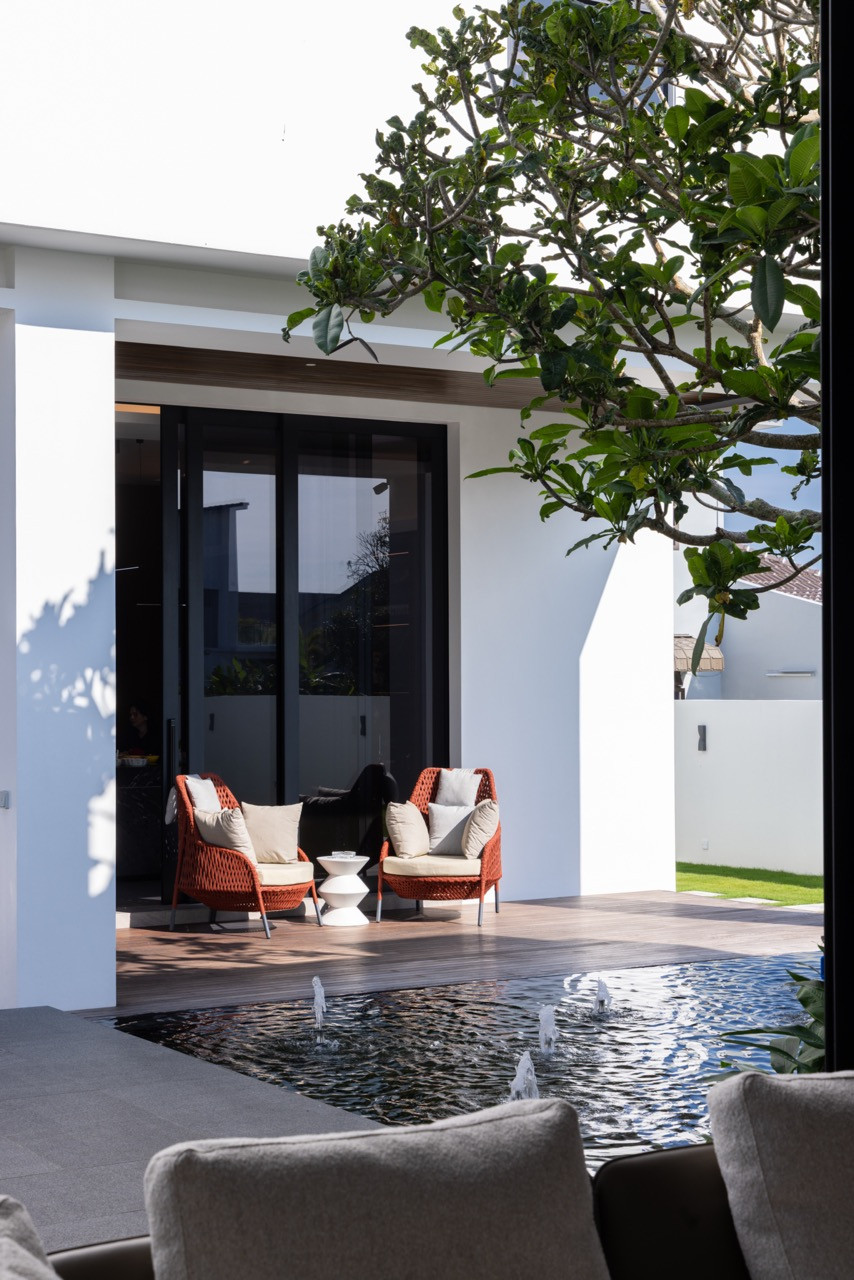 The rear villa terrace, with two red woven chairs positioned at the pond edge beside the frangipani tree