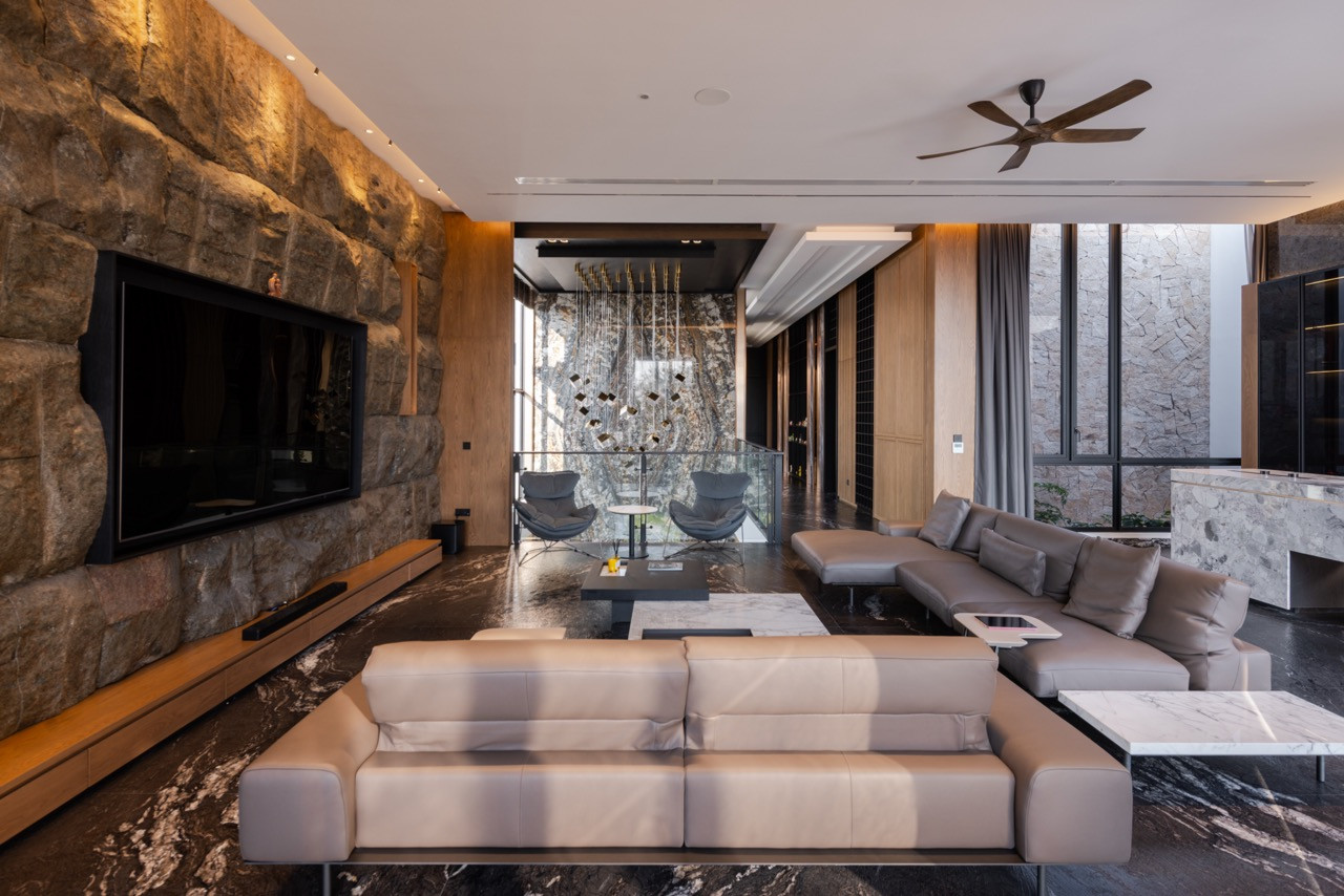 The main living room in full, showing the rough-split granite wall on the left, Titanium Antique marble flooring, and the internal courtyard visible through full-height glazing to the right