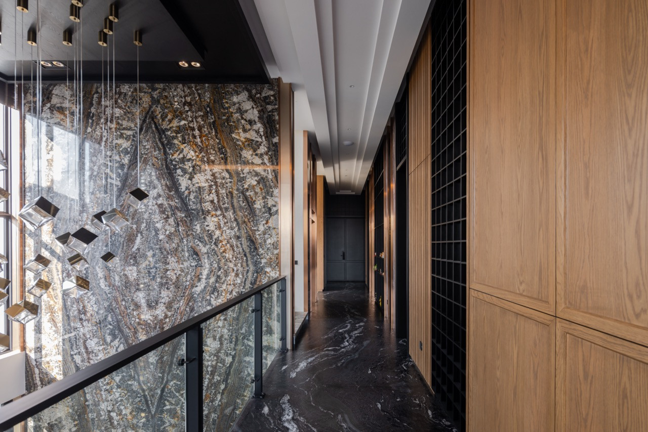 The first-floor corridor runs alongside the Olive Wave Granite slab, with solid timber joinery cabinetry lining the opposite wall and dark marble floors below