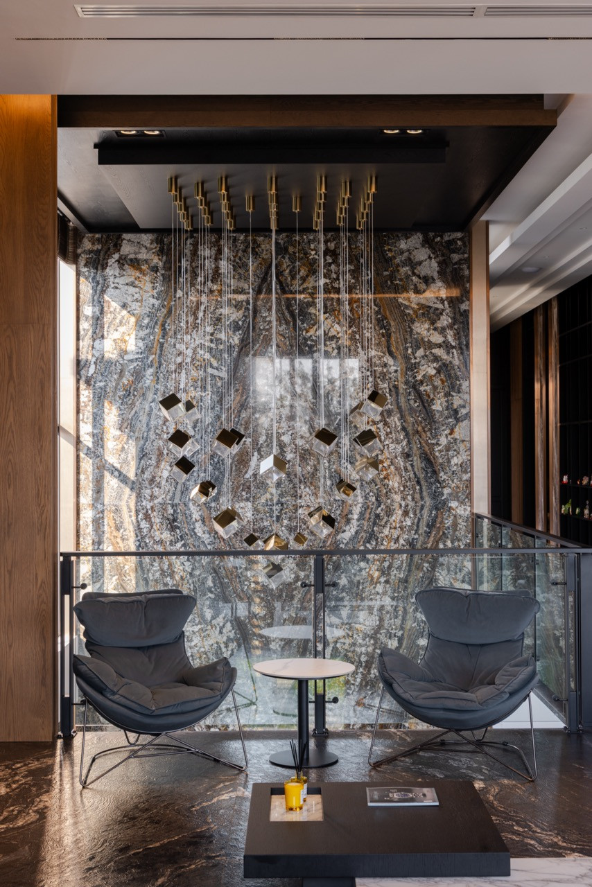 A pair of lounge chairs occupies the mezzanine landing, set against the bookmatched Olive Wave Granite feature wall