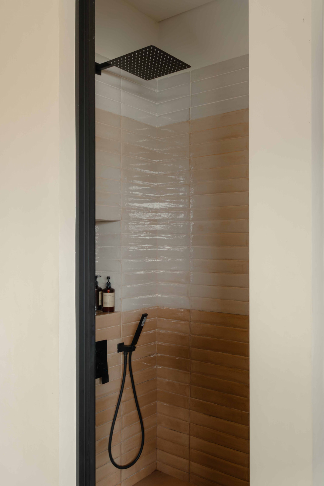 A peek into the shower area reveals glossy white tiles in crisp contrast to the surrounding terracotta tones