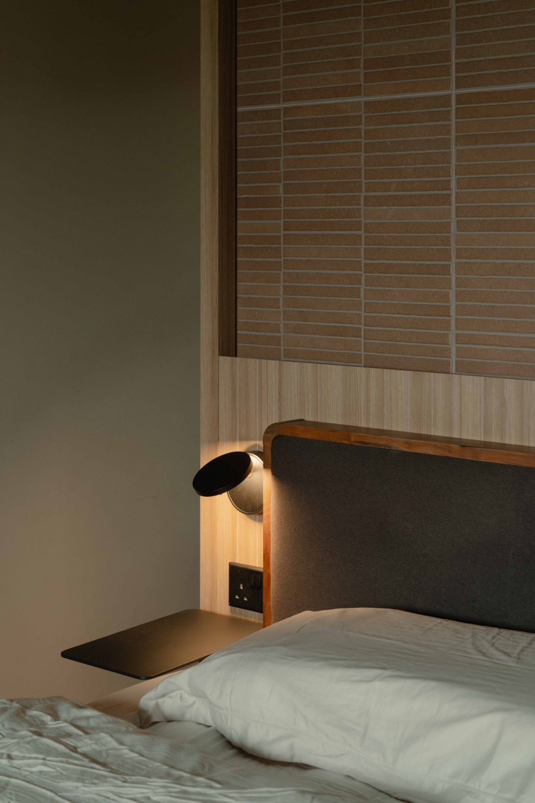 A bedside vignette pairs a sculptural lamp with a brick finish backdrop above the bedhead