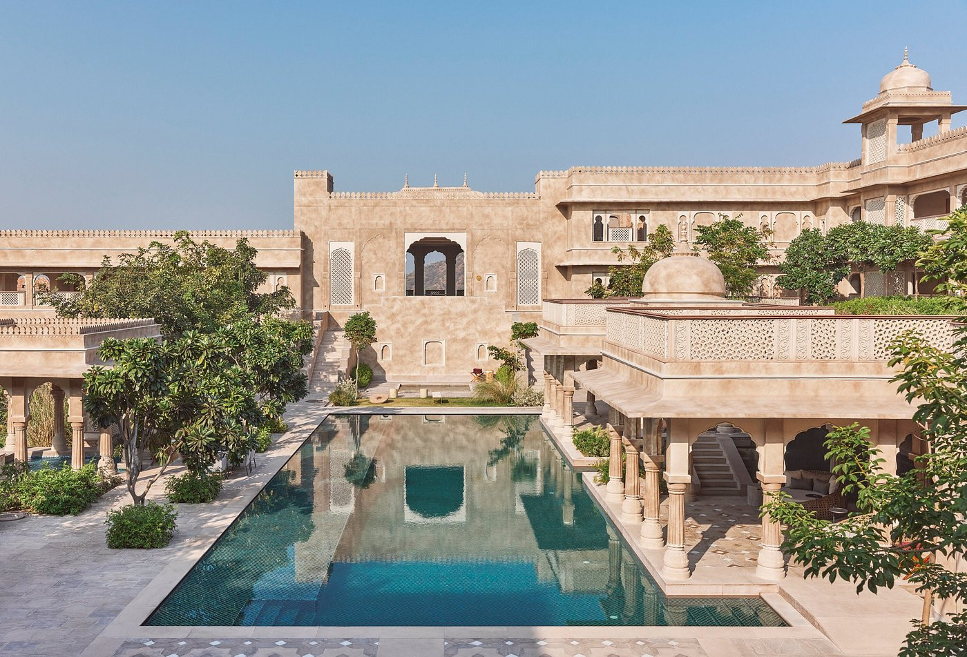 The Rani Bagh pool courtyard at Six Senses Fort Barwara, Rajasthan, is framed by sandstone arcades and the fort's original battlemented walls