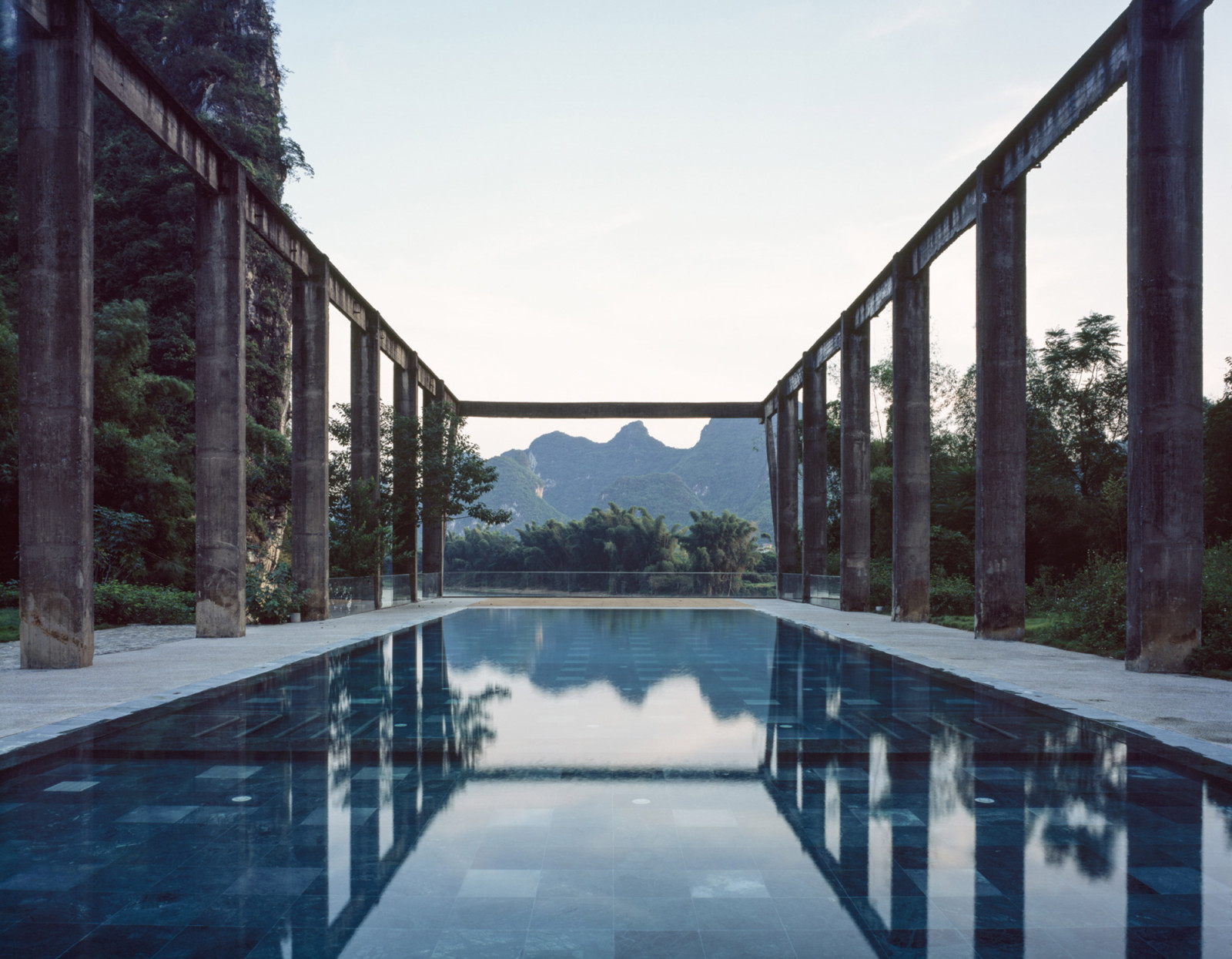 The swimming pool occupies the former sugarcane loading dock, framed by the mill’s original concrete truss structure with karst mountains visible beyond