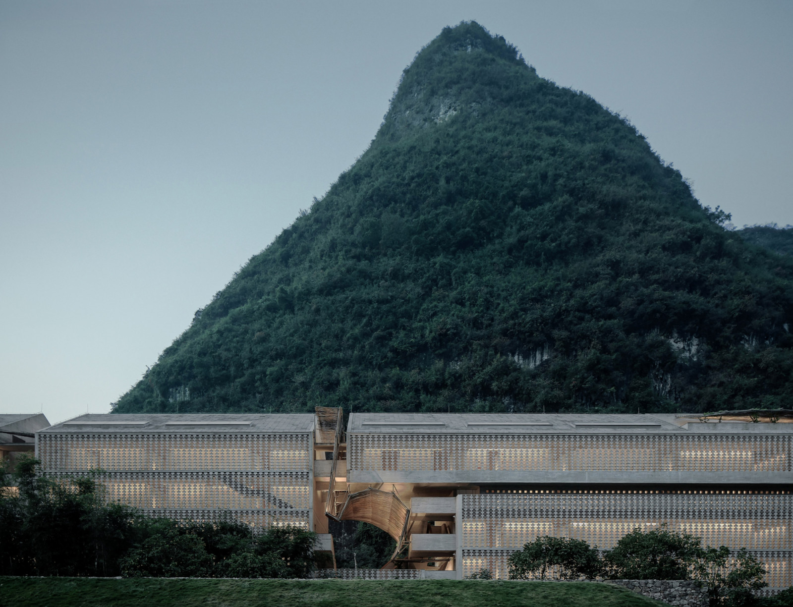 The new guest room building by Vector Architects has a perforated concrete block facade set against one of Yangshuo’s characteristic karst peaks; the bamboo entrance structure rises at the centre