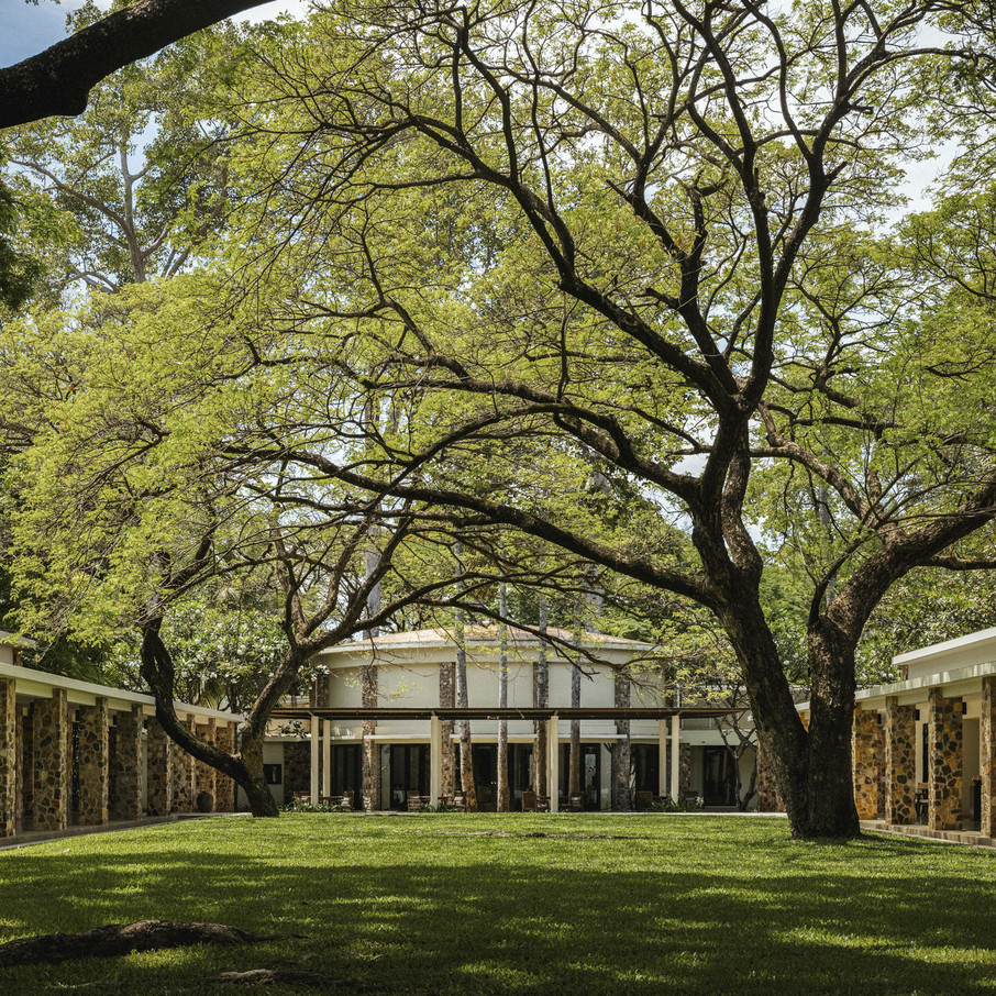 The central lawn at Amansara, Siem Reap, framed by the low-slung collonaded wings of Laurent Mondet’s 1962 compound; the canopy of mature trees is original to the Villa Princière estate