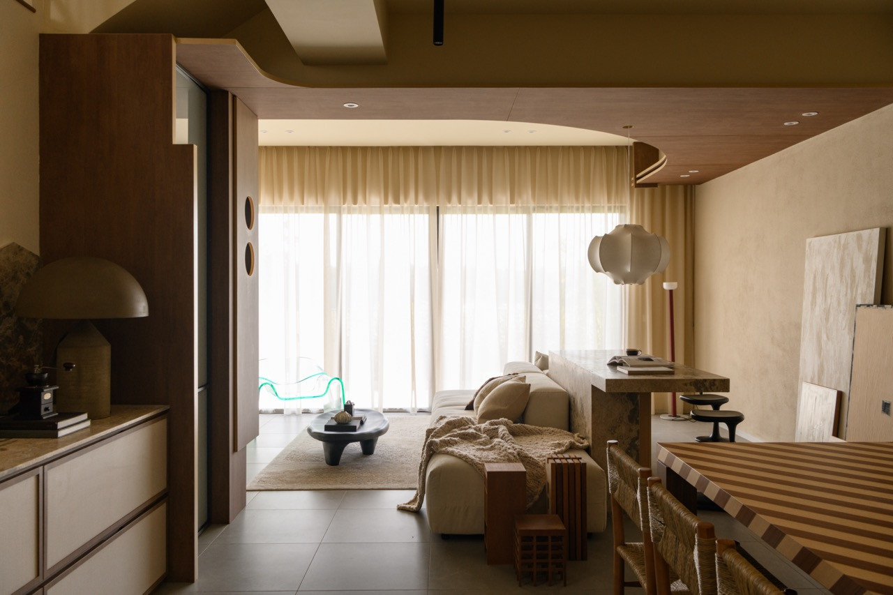 The open-plan ground floor with the living and dining areas visible together, the curved wood ceiling, striped dining table, and floor-to-ceiling glass doors dressed with sheer curtains