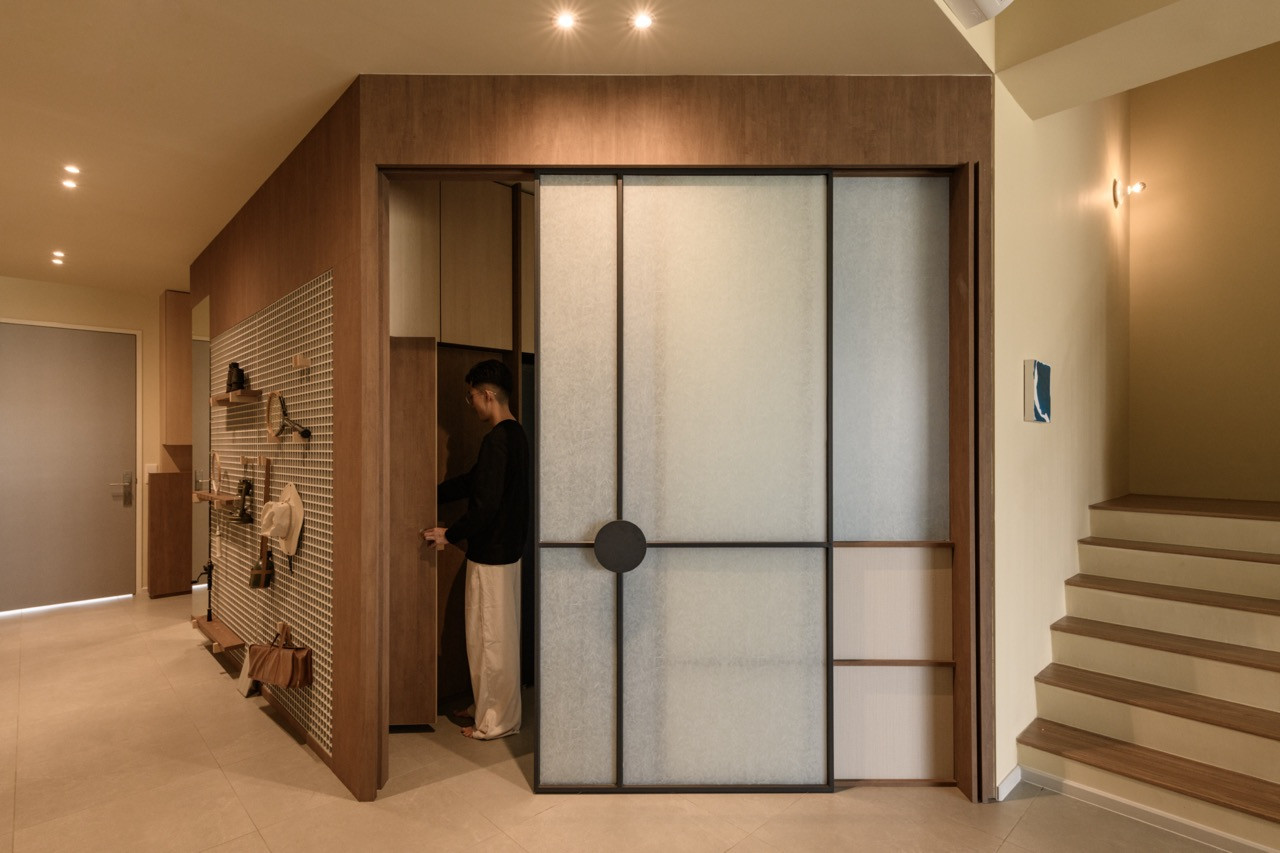 The ground-floor entrance with a large sliding door in a dark wood frame with frosted panels and a circular handle, alongside a gridded wall panel fitted with hooks and shelves
