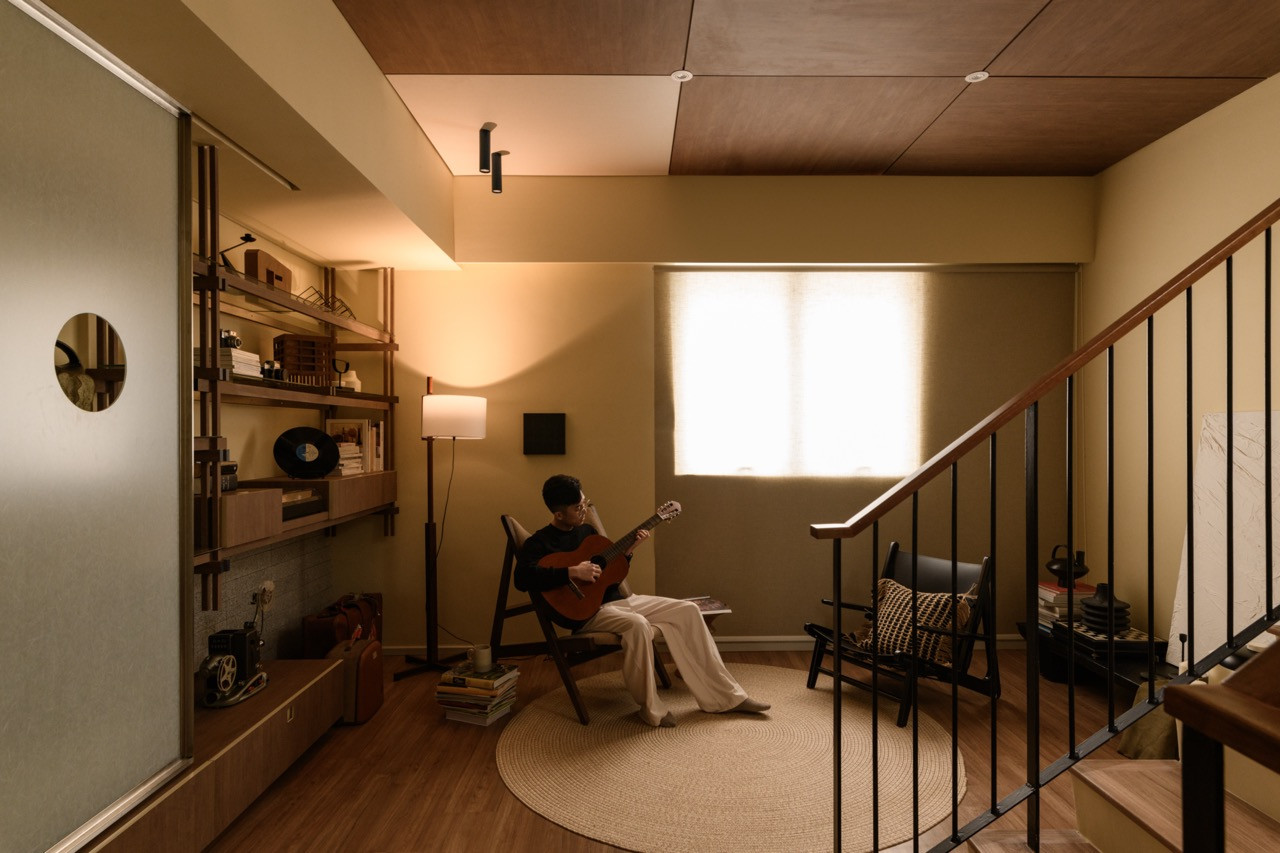 The first-floor landing with a pair of easy chairs on a round jute rug, floor lamp, open shelving, and a wood-panelled ceiling above the staircase