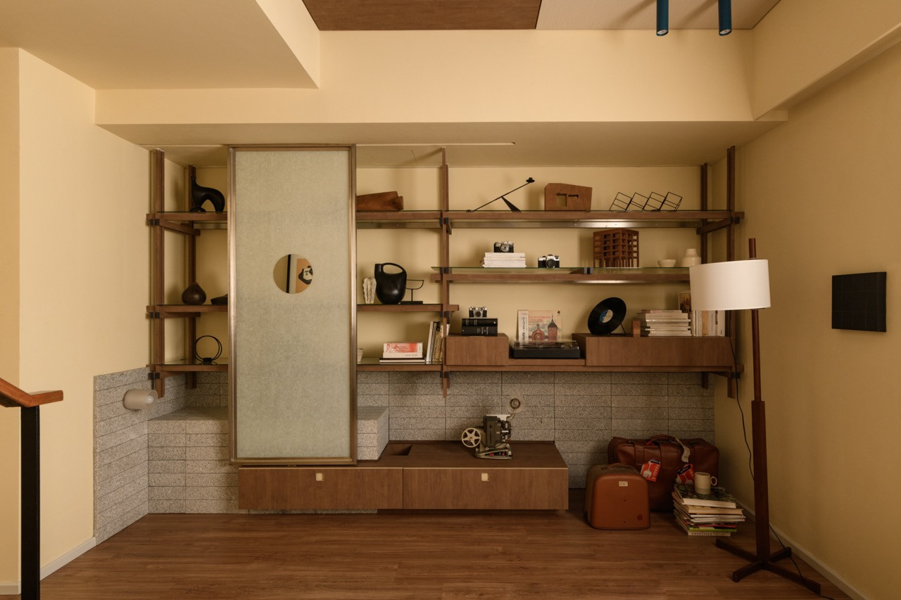 The first-floor chill-out area features a full-height open shelving system in dark wood set against a granite tile base, displaying books, a vintage camera, and a film projector